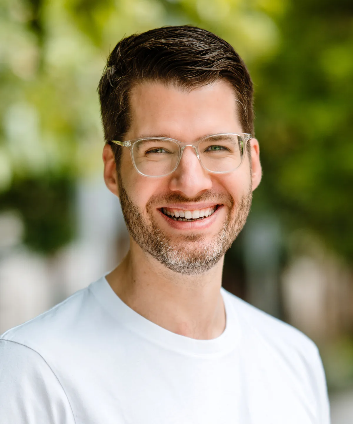 Philip Stanislaus, smiling, in glasses and a white T-shirt, outdoors.